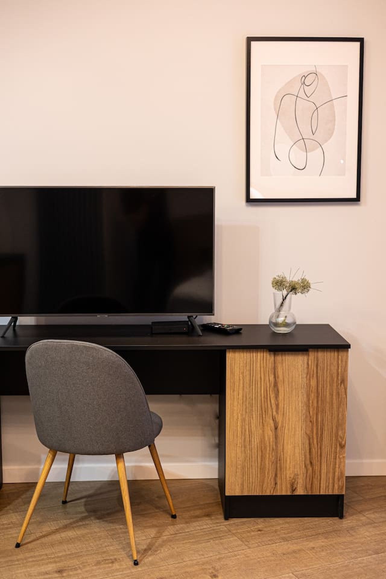 A modern room with a flat-screen TV, a grey chair, a wooden side table, and a framed abstract art piece.