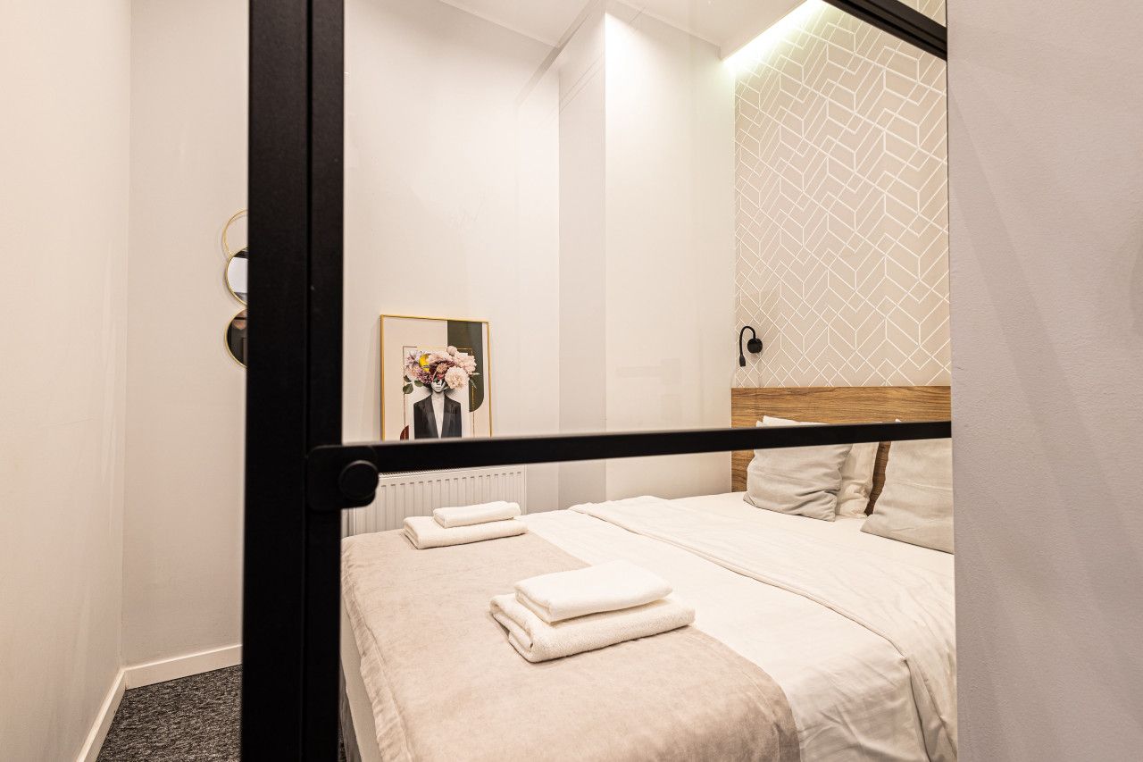 Una habitación de hotel con cama, toallas, un cuadro enmarcado y un papel tapiz estampado.