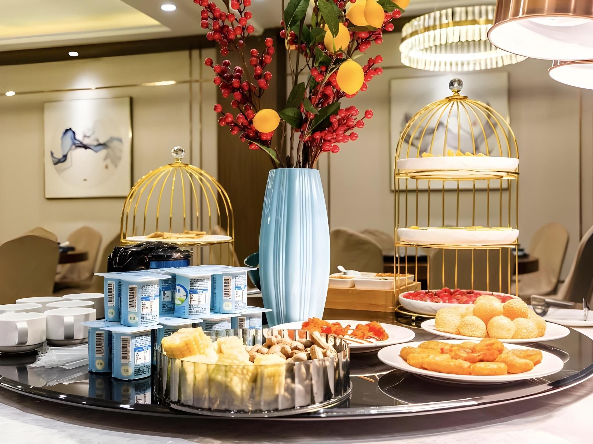 A buffet setup with various food items, a decorative vase with flowers, and two gold-framed light fixtures.