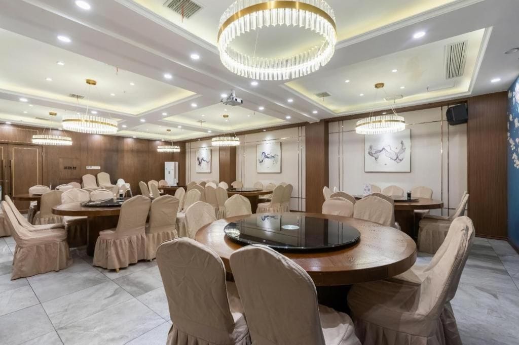 A conference room with round tables, beige chairs, and chandeliers.