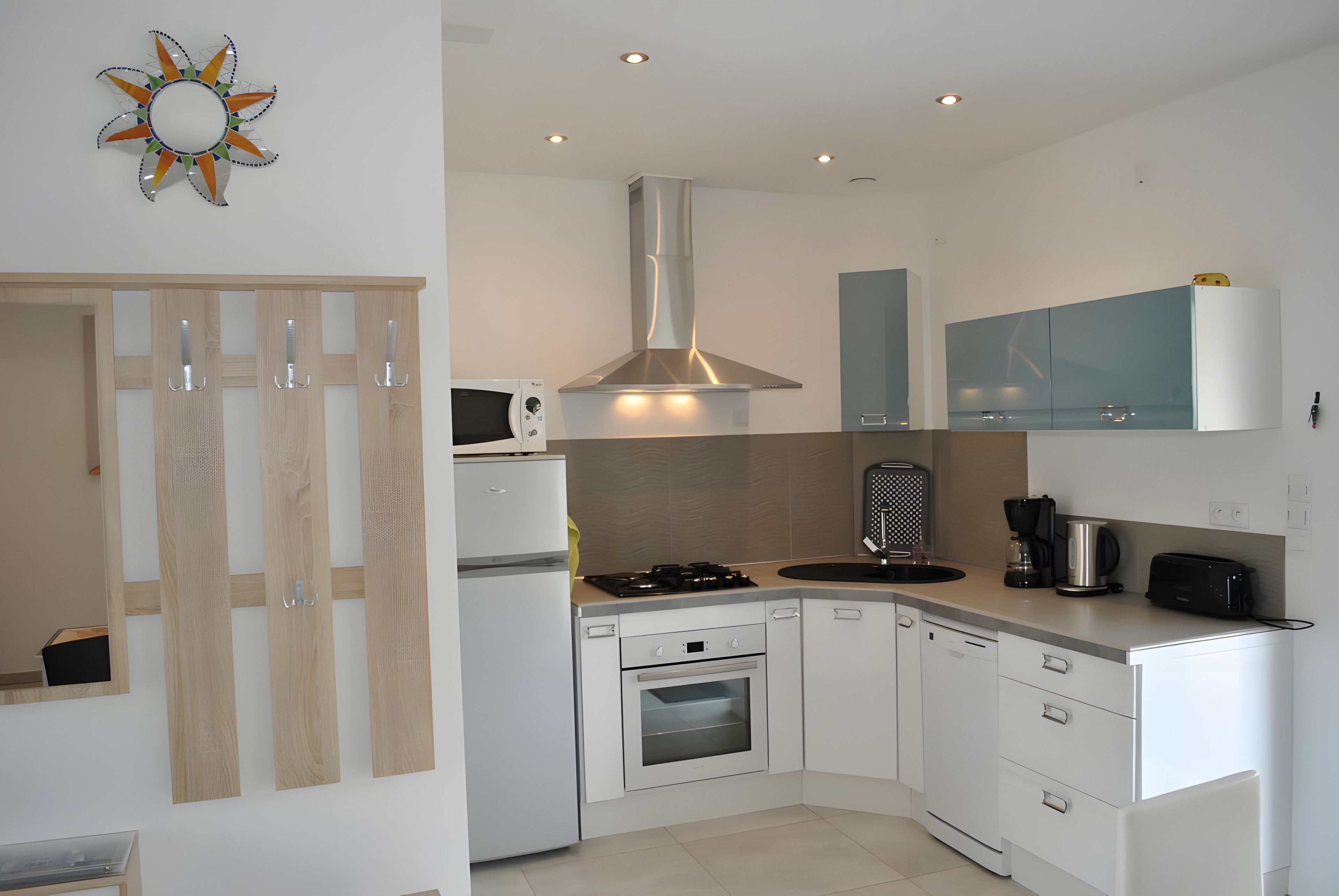 A modern kitchen with white cabinetry, a stainless steel range hood, a built-in oven, and a large window.