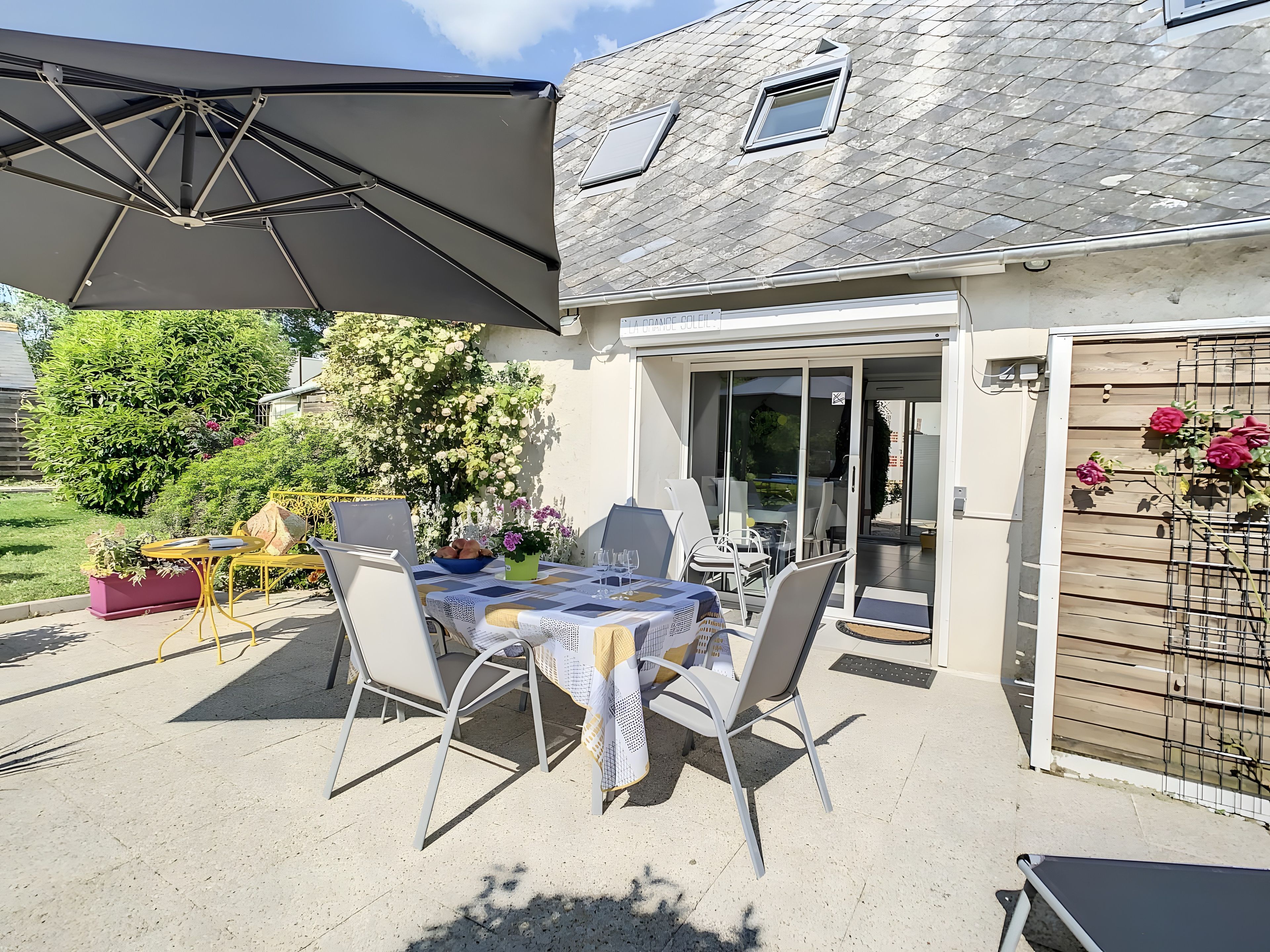 Une terrasse extérieure avec une table dressée pour le repas, des chaises et un grand parasol.
