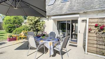 Une terrasse extérieure avec une table dressée pour le repas, des chaises et un grand parasol.