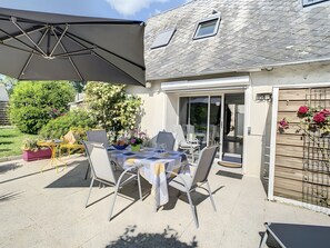 An outdoor patio with a table set for dining, chairs, and a large umbrella.