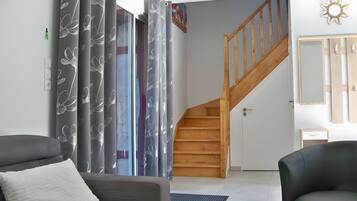 A modern living room with a grey sofa, a black armchair, a wooden staircase, and grey curtains with a floral pattern.