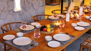 Una mesa de comedor dispuesta con platos, vasos y una cesta de frutas, rodeada de sillas.