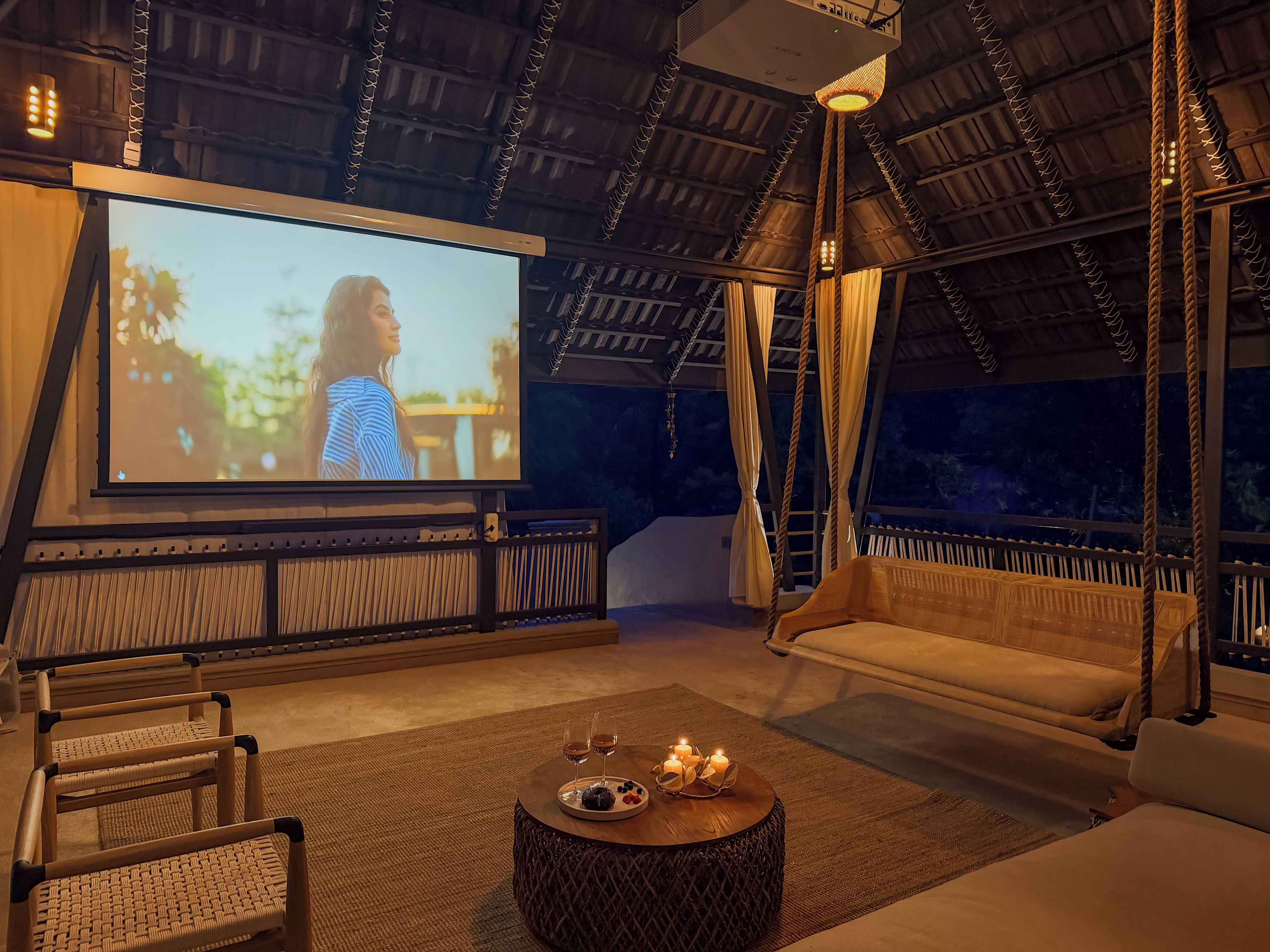 Una habitación acogedora con una pantalla grande, asientos cómodos y una mesita con bebidas y velas.