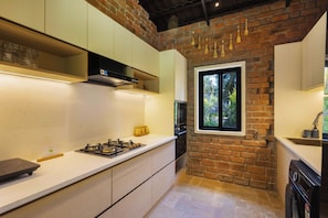 A kitchen with a brick wall, a window, and a modern stove. - ELIVAAS Prive Saukhyam 3BHK Villa (Bengaluru)