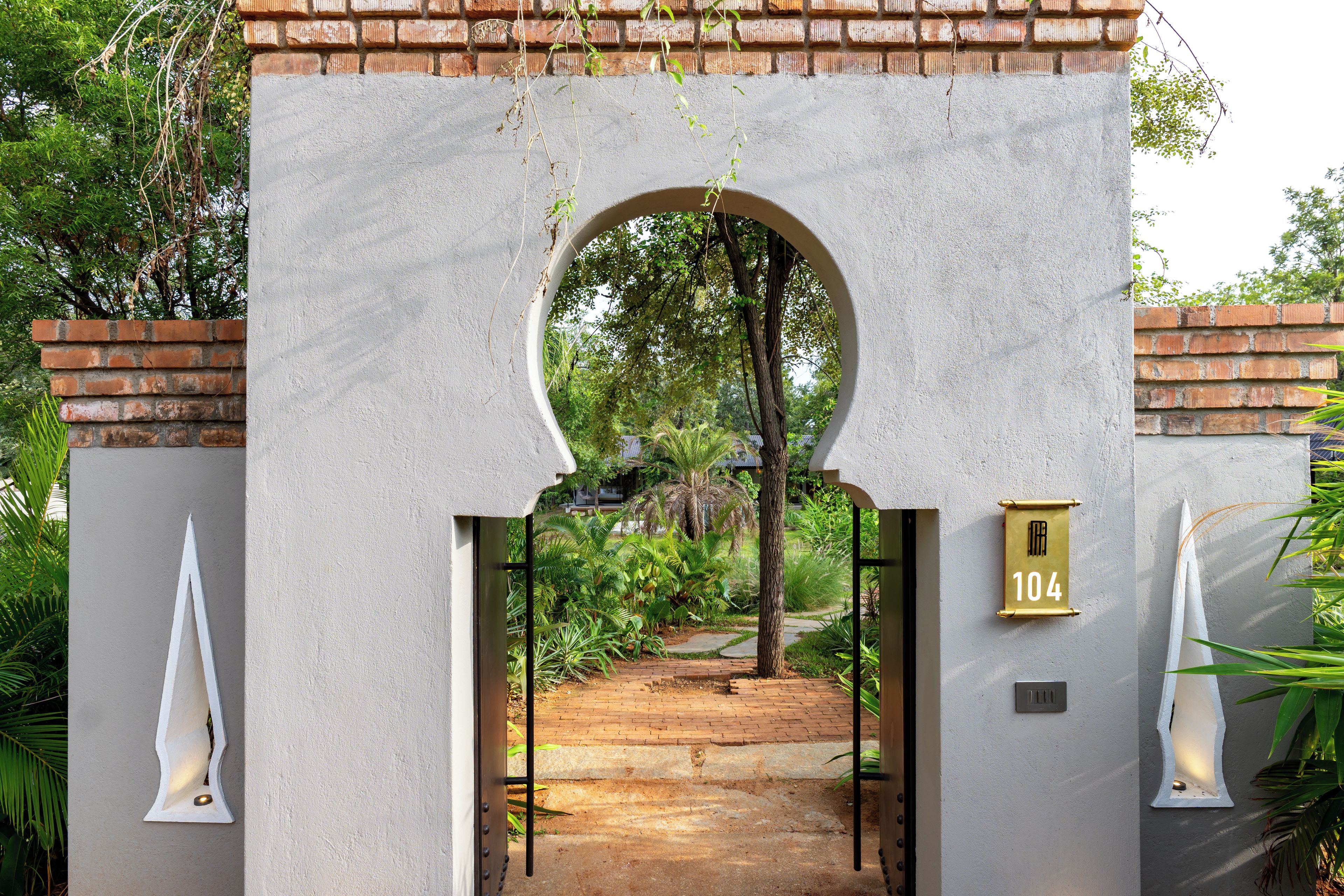 A gated entrance with a brick wall, a number sign, and a pathway leading into a lush garden.