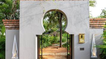 A gated entrance with a brick wall, a number sign, and a pathway leading into a lush garden.