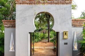 A gated entrance with a brick wall, a number sign, and a pathway leading into a lush garden. - ELIVAAS Prive Saukhyam 3BHK Villa (Bengaluru)