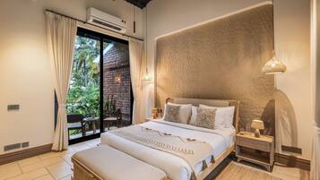 A bedroom with a large bed, a view of greenery outside, and a brick wall.
