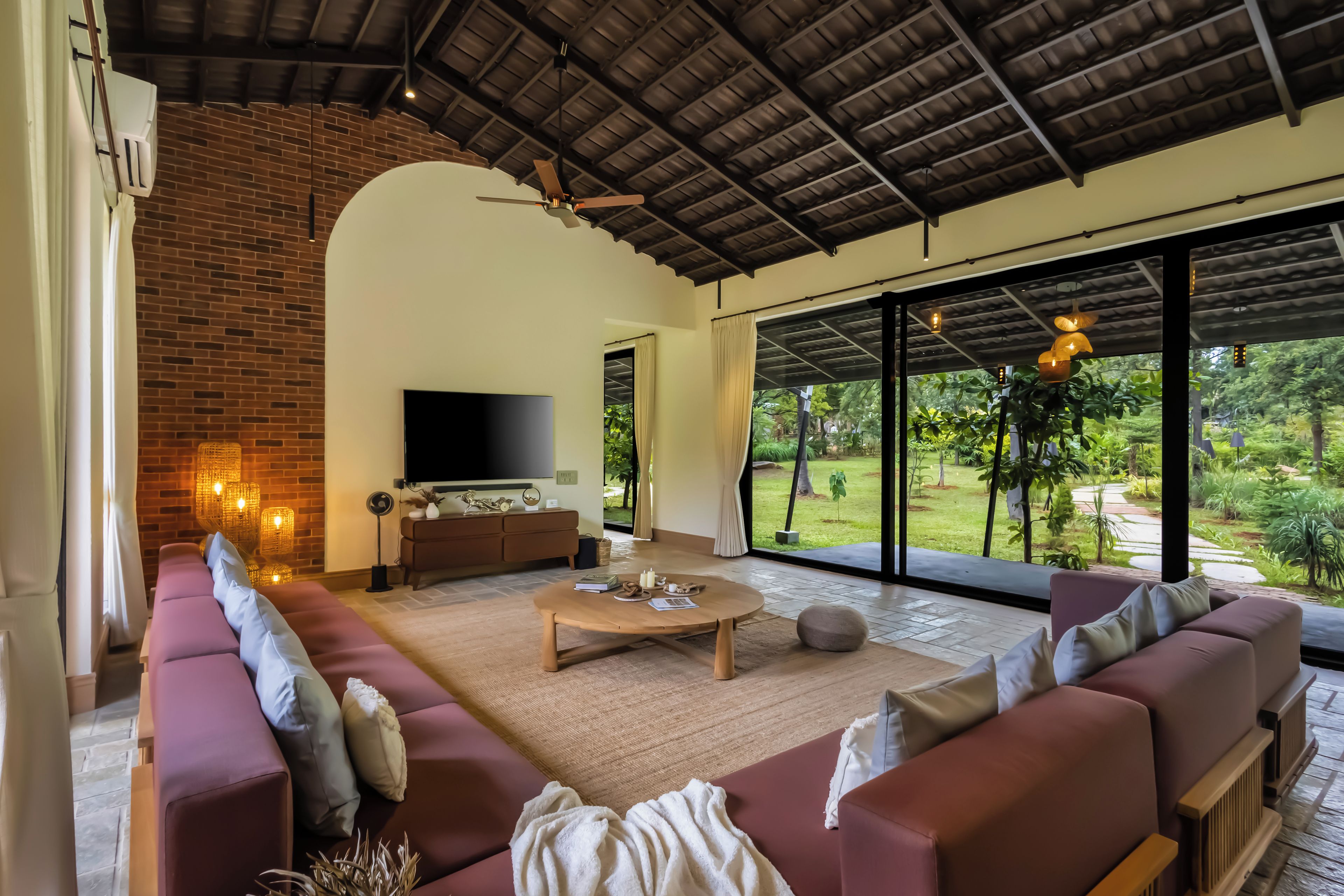 A spacious living room with a large TV, comfortable seating, and a view of a lush garden.