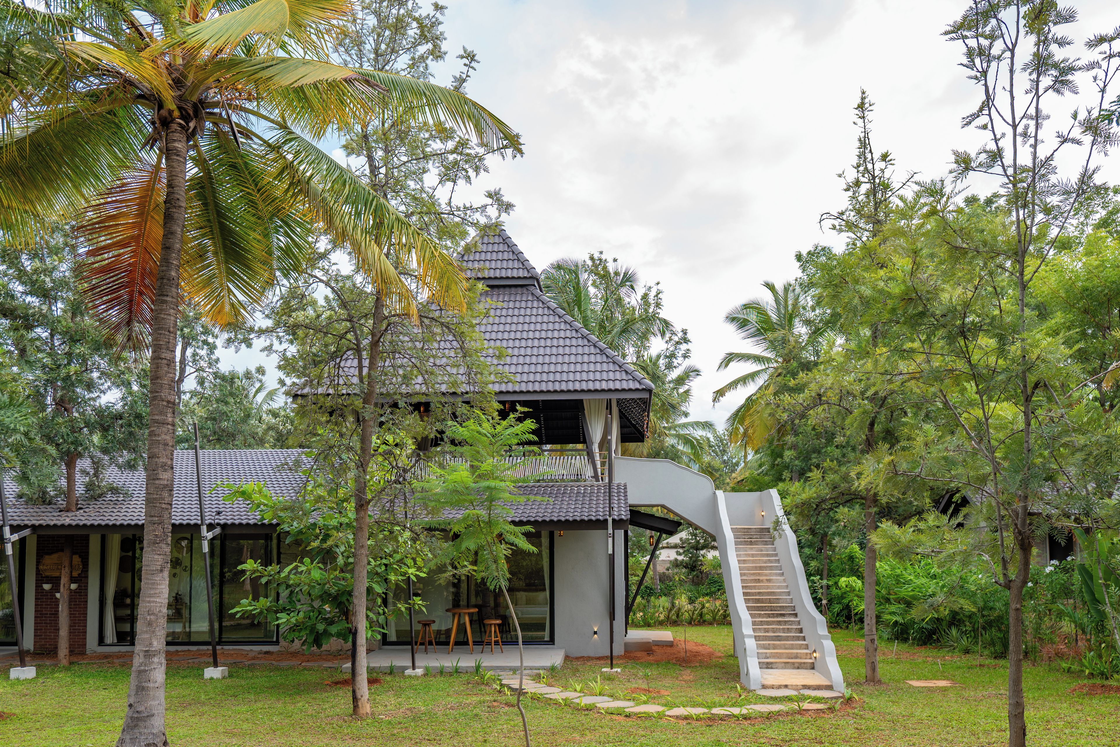 A modern house with a steep staircase leading to a balcony, surrounded by lush greenery.