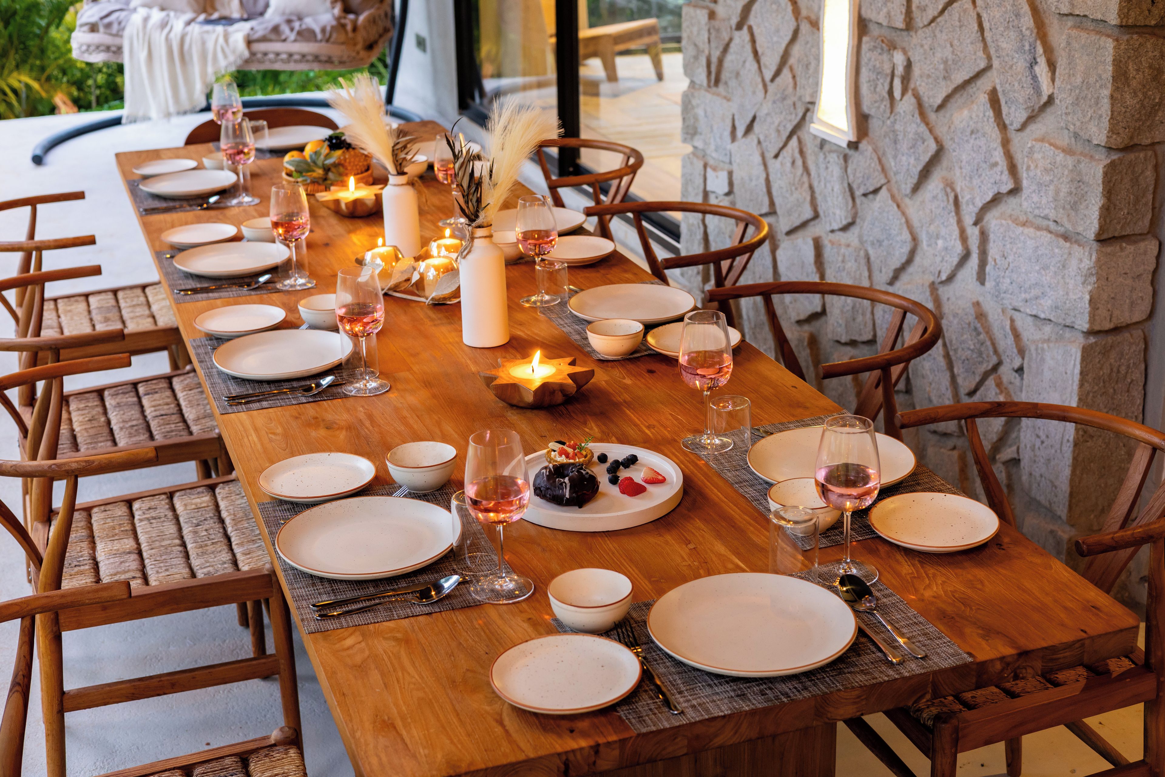 A long wooden dining table set for a meal with candles, plates, and glasses.
