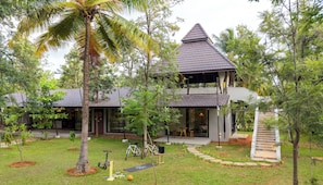 A two-story house with a balcony, surrounded by trees and a well-maintained lawn. - ELIVAAS Prive Saukhyam 3BHK Villa (Bengaluru)