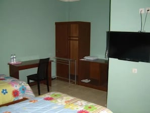 A small room with a bed, a desk, a chair, a wardrobe, and a refrigerator. - Nirwarna Hotel Bojonegoro (Bojonegoro)