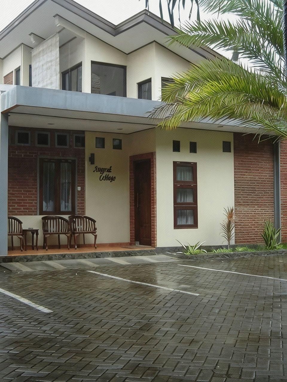 A two-story building with a brick facade, a covered entrance with wooden chairs, and a sign that reads 'Angkar Atma.'