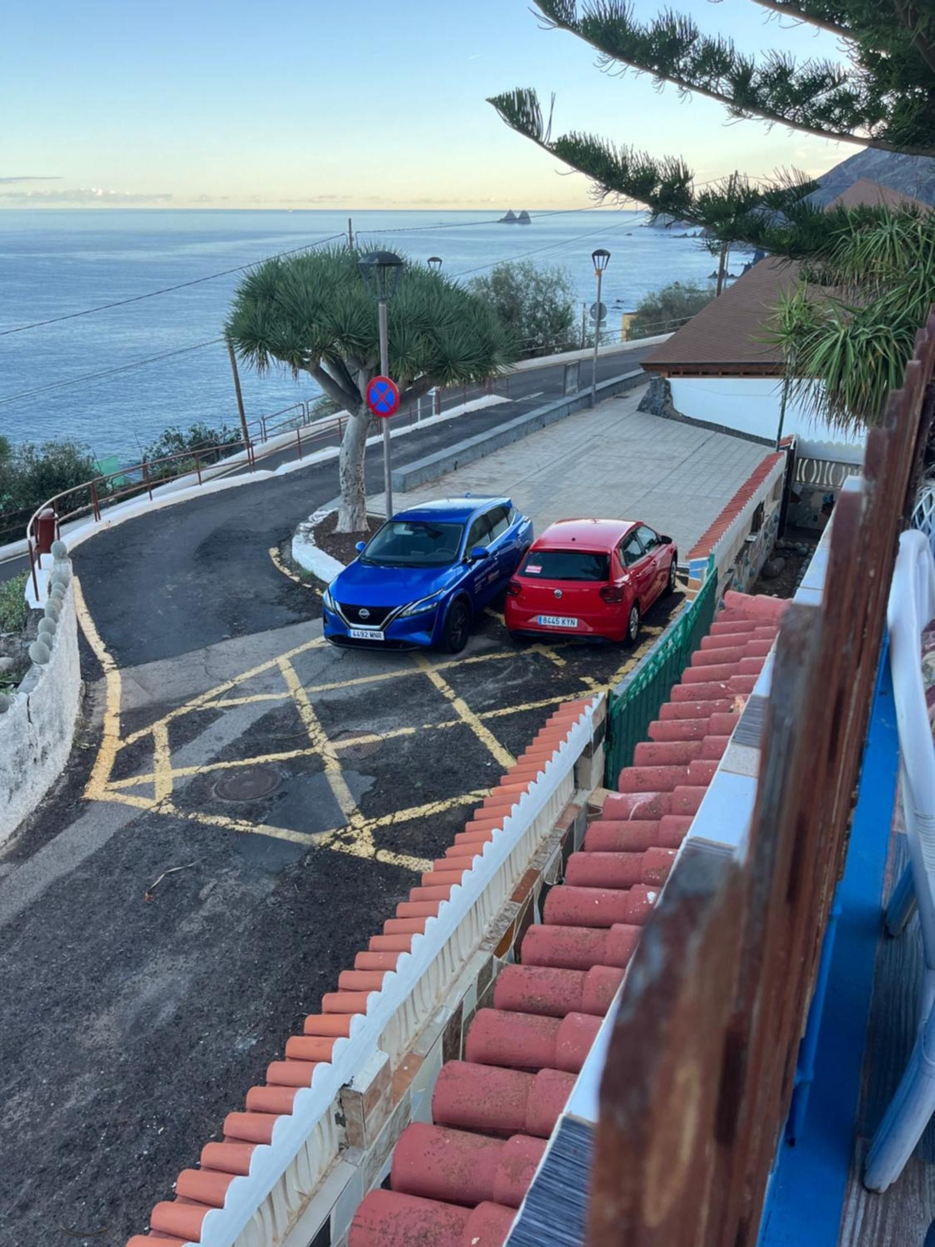 Una carretera costera con dos autos estacionados, una señal de prohibido estacionar y vista al mar.