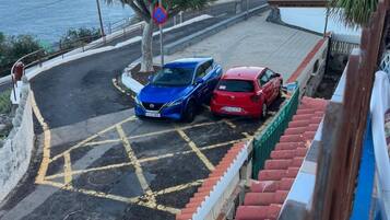 Una carretera costera con dos autos estacionados, una señal de prohibido estacionar y vista al mar.