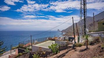 A coastal view with a clear sky, a tennis court, and a mountain in the background.