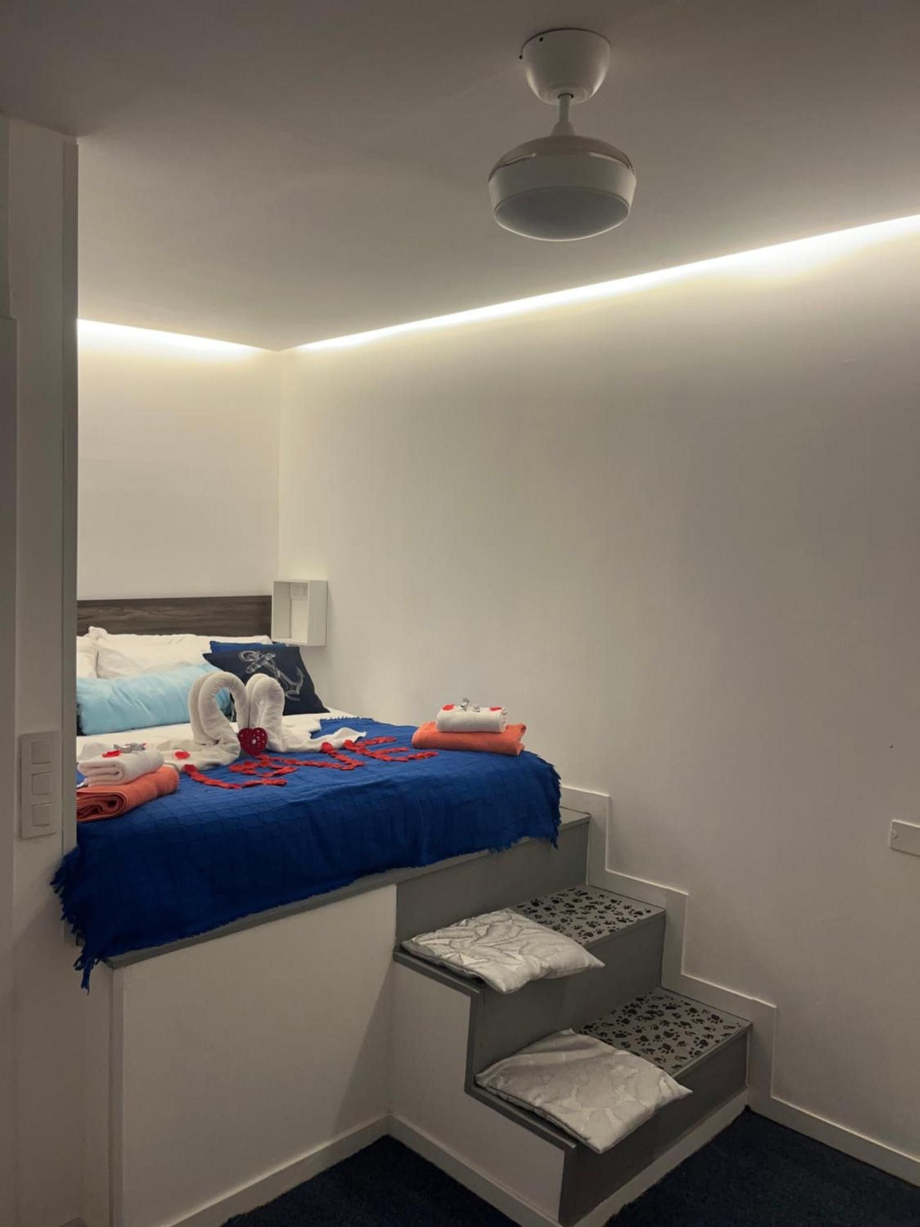 Een hotelkamer met een stapelbed, een klein bureau, een stoel, een nachtkastje en een plafondventilator.
