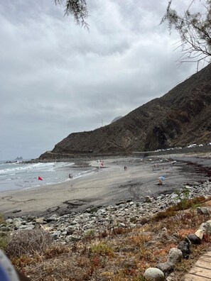 A beach with rocky terrain, a red flag indicating a warning, and a mountainous backdrop.