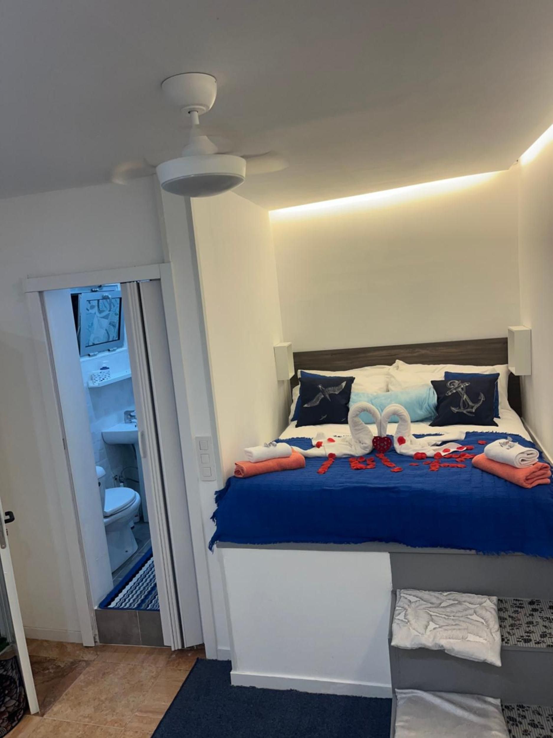 Ein Hotelzimmer mit einem Bett, einem Deckenventilator, einem durchgegangene Tür sichtbaren Badezimmer und einem kleinen Teppich auf dem Boden.