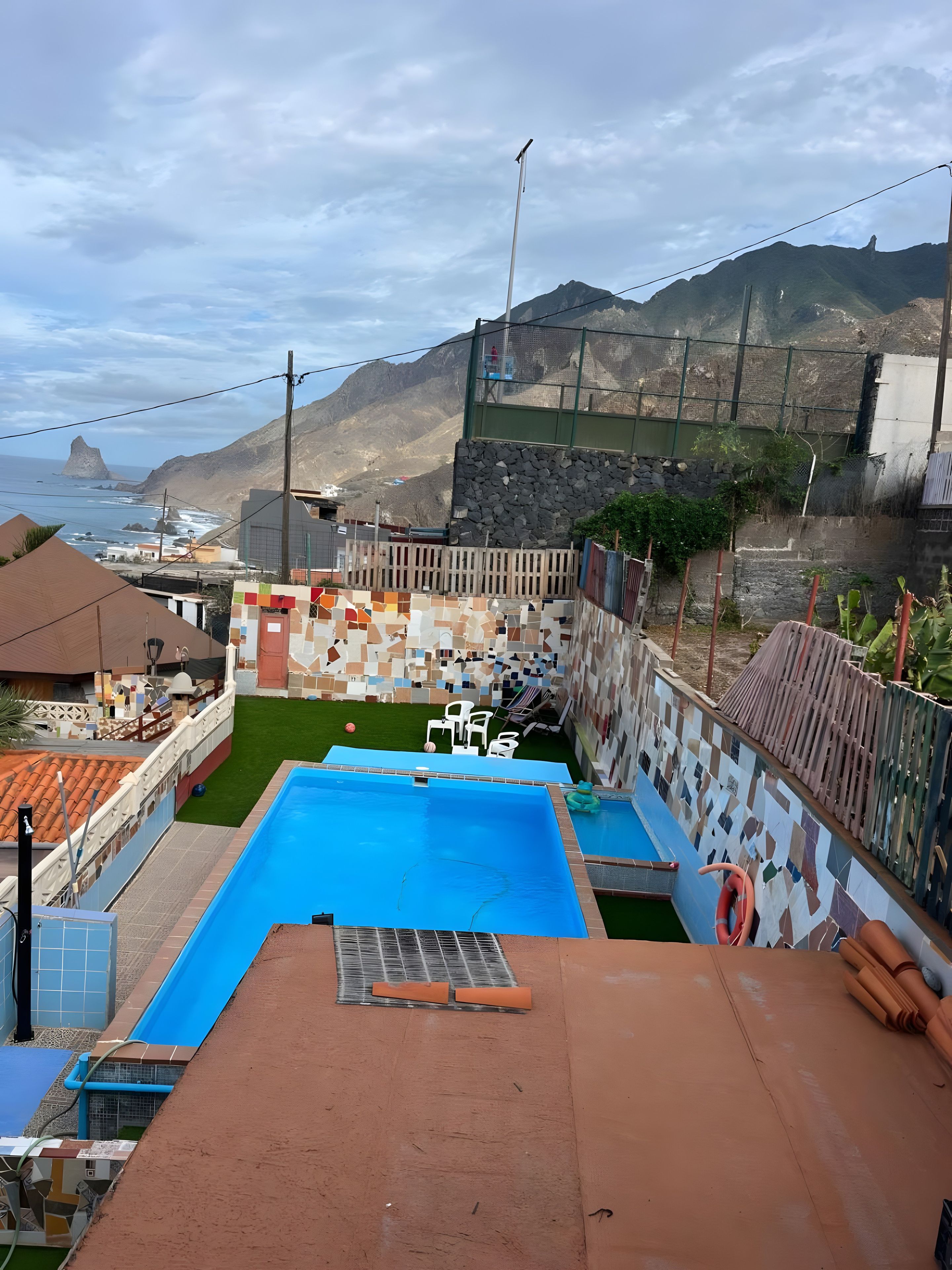 Une piscine avec un toboggan, entourée d ’une zone délimitée par une clôture, offrant une vue sur l’océan et les montagnes.
