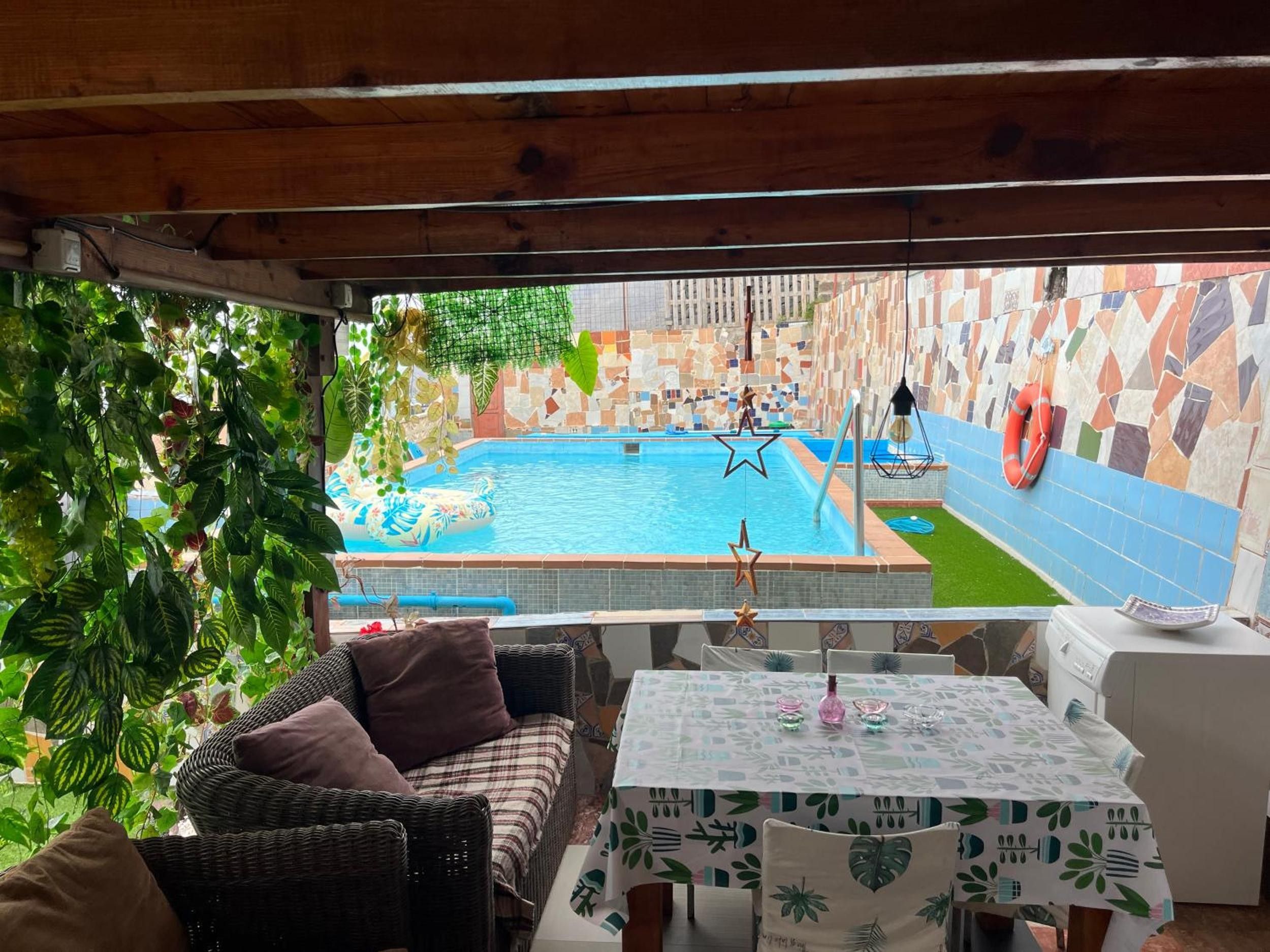 A pool area with a view of a cityscape, a wicker sofa, a table with a patterned tablecloth, and a tiled wall.