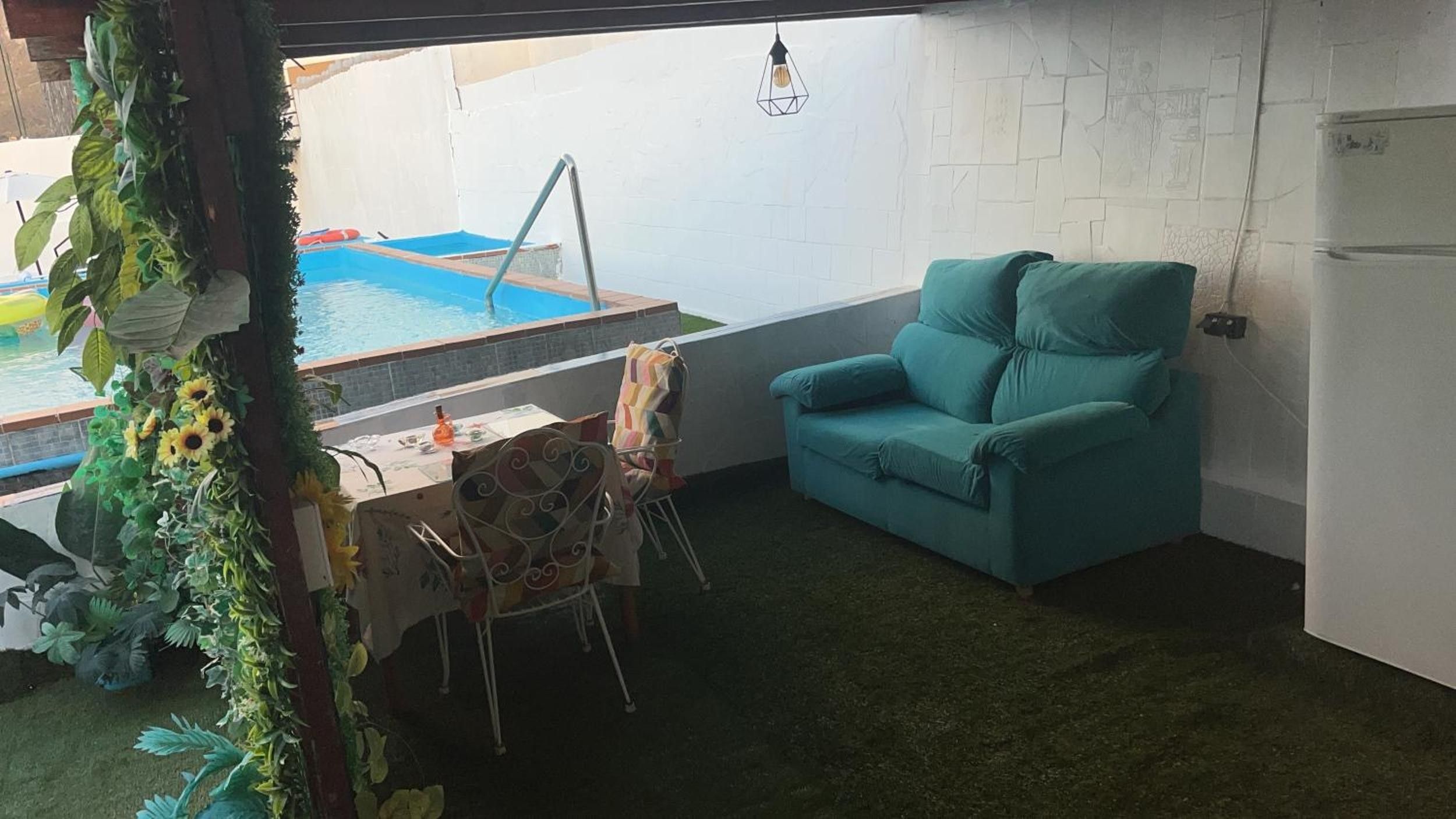 A small room with a pool, a teal chair, and a table with a chair.