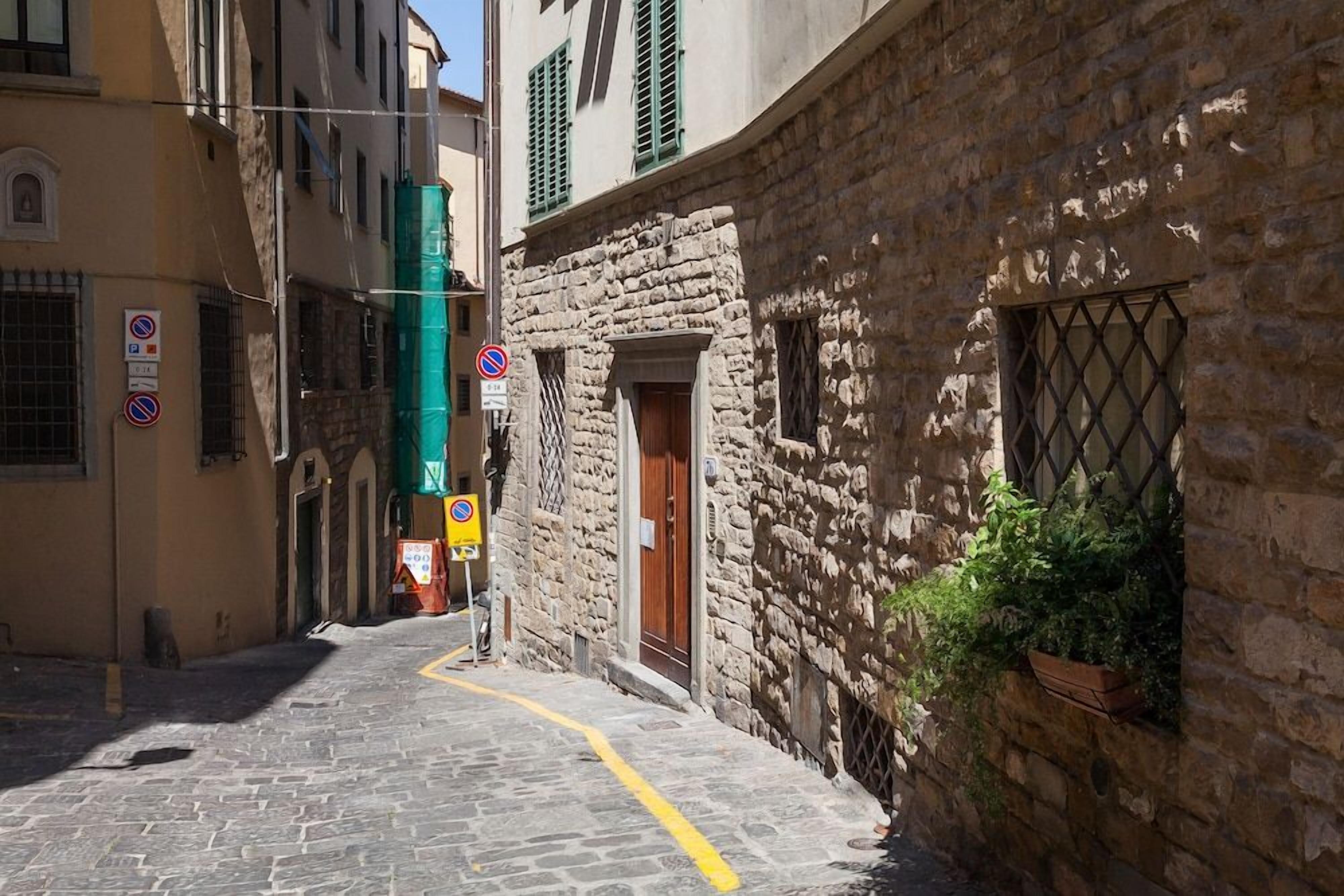 A narrow cobblestone street flanked by historic stone buildings with barred windows and a yellow line marking the path.