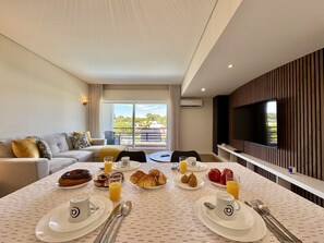 A modern hotel room with a dining area, a sofa, a TV, and a balcony with a view. - VILAMOURA GOLF APARTMENT 4 WITH POOL by HOMING (Vilamoura)