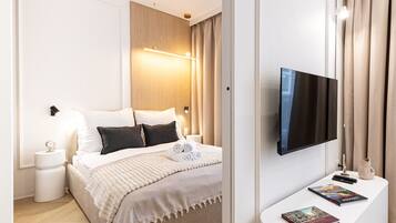 Una habitación de hotel moderna con cama, mesita de noche, lámpara, televisor y una pequeña mesa con libros.