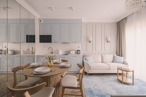 Une cuisine moderne avec des meubles de couleur bleu clair, un coin repas doté d’une table ronde et un salon avec un canapé beige.