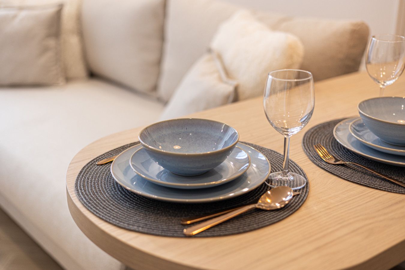 Een eettafel gedekt met blauwe kommen, borden, een wijnglas en bestek op een ronde tafel met een geweven placemat.