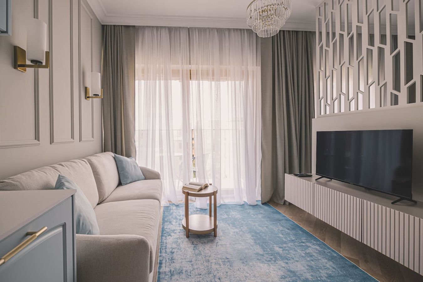 Ein modernes Wohnzimmer mit einer Couch, einem Fernseher, einem kleinen Tisch und transparenten Vorhängen.
