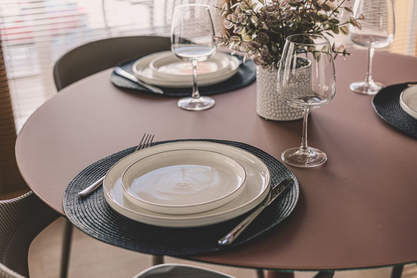 Una mesa redonda lista para comer, con platos, cubiertos y vasos.