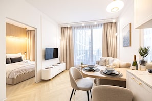 Ein modernes Hotelzimmer mit Bett, Fernseher, Esstisch mit Stühlen, einer Sitzecke und Blick auf die Stadt.