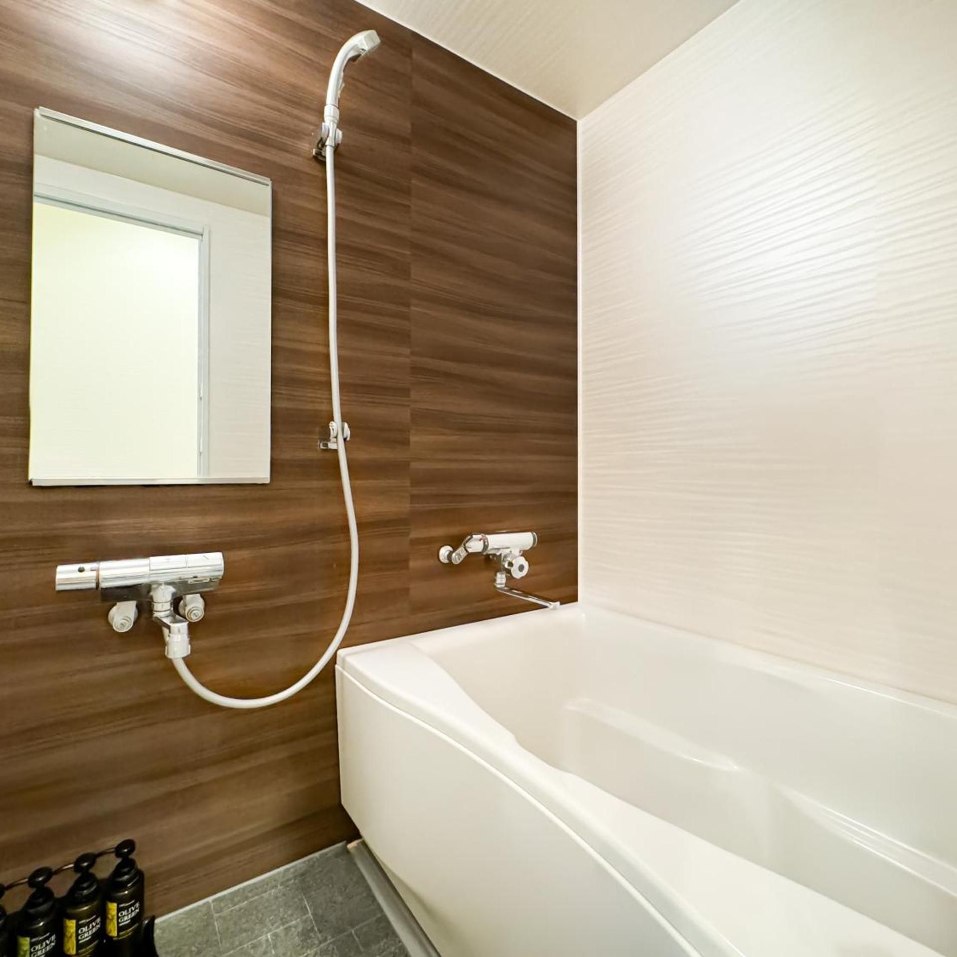 A modern bathroom with a white bathtub, wooden wall paneling, a mirror, and a showerhead.