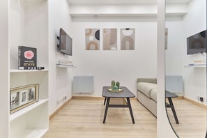 Ein modernes Wohnzimmer mit Flachbildfernseher, Bücherregal mit Büchern, Couchtisch mit Dekoration und einer Couch.