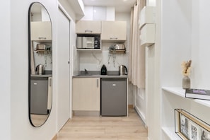 Eine kompakte Küche mit Mikrowelle, Toaster und Wasserkocher auf der Arbeitsfläche, einem kleinen Kühlschrank und einem Spiegel an der Wand.