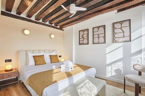 Un dormitorio moderno con techo de madera, cama con ropa de cama blanca, manta marrón y una silla.