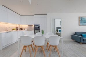 Una cocina moderna con armarios blancos, una mesa de comedor con sillas y un sofá gris en la sala.
