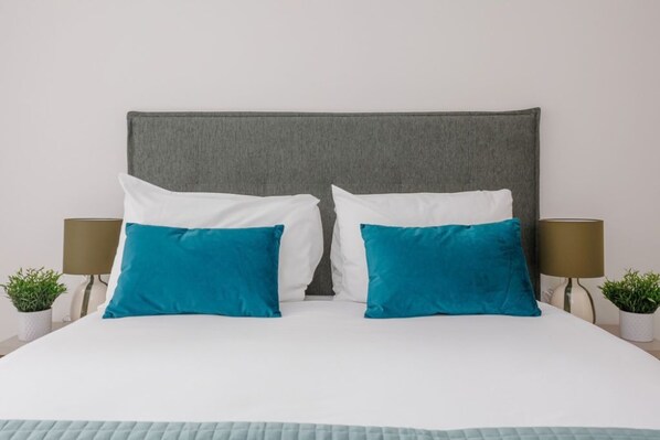 Una cama con cabecera gris, almohadas blancas y turquesa, y una colcha acolchada.