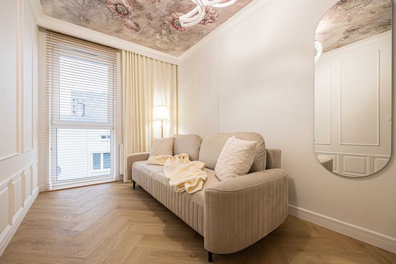 Una sala de estar moderna con un sofá, un espejo y vistas al exterior a través de una ventana con persianas.