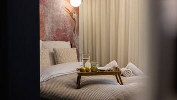 Een opgemaakt bed met een dienblad met citroenen en een glas water, een hangende lamp en een structuurmuur.