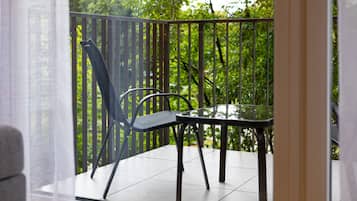 Un balcón con una mesa de vidrio y sillas de metal, rodeado por una valla de madera y vegetación.