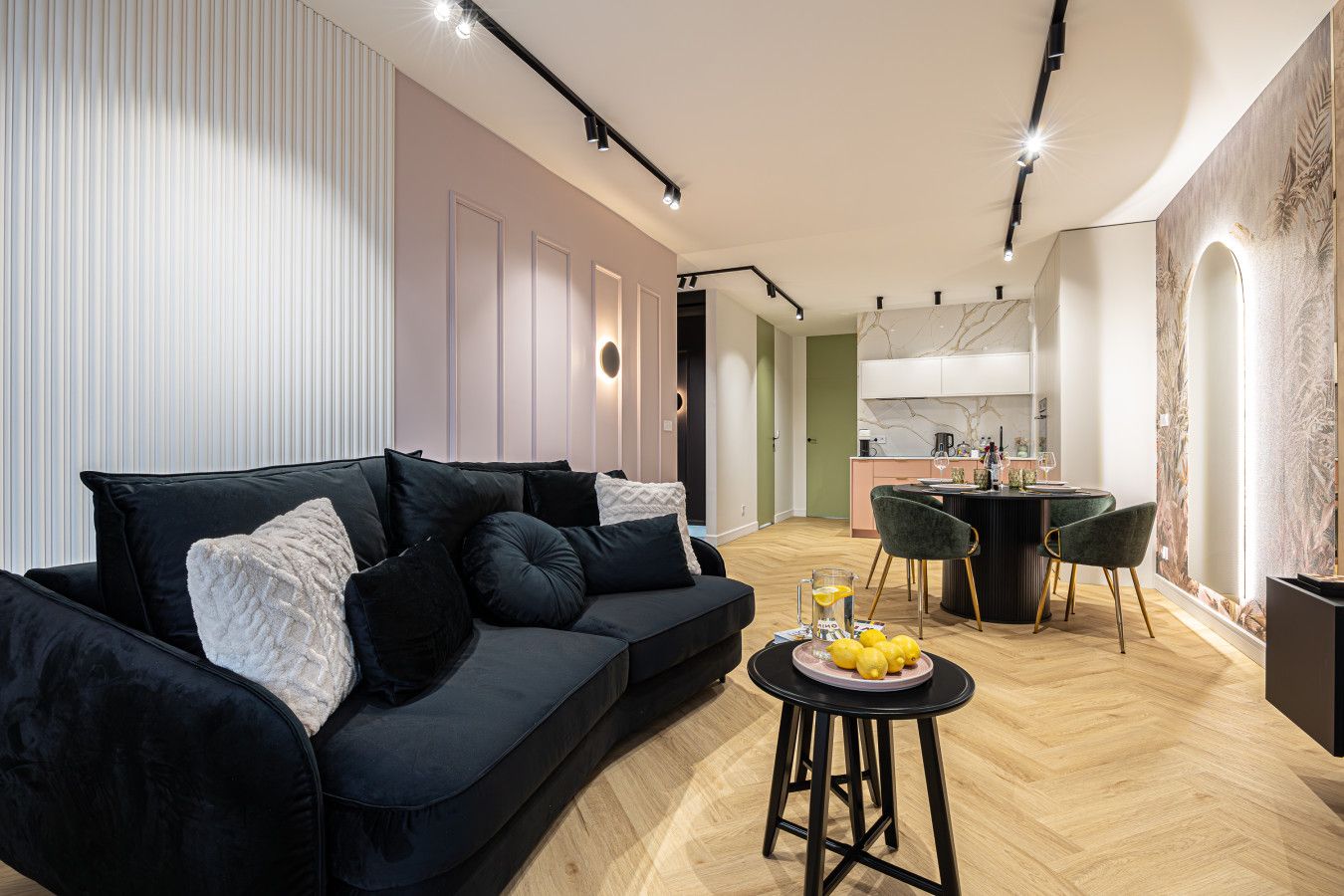 Una sala de estar moderna con un sofá negro, una mesita redonda con limones y una cocina al fondo.