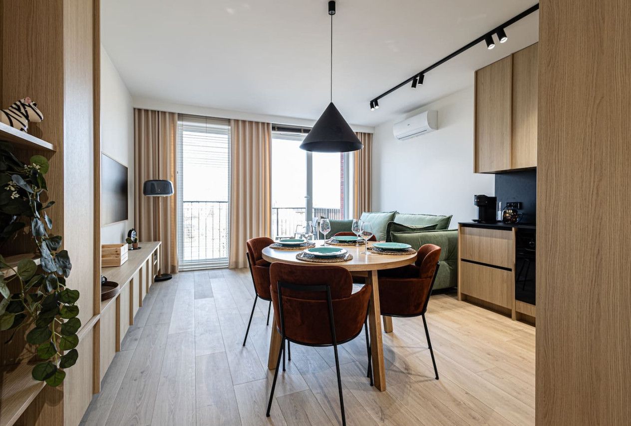 Una cocina moderna con armarios de madera, un comedor con una mesa redonda y sillas, y un ventanal con cortinas.